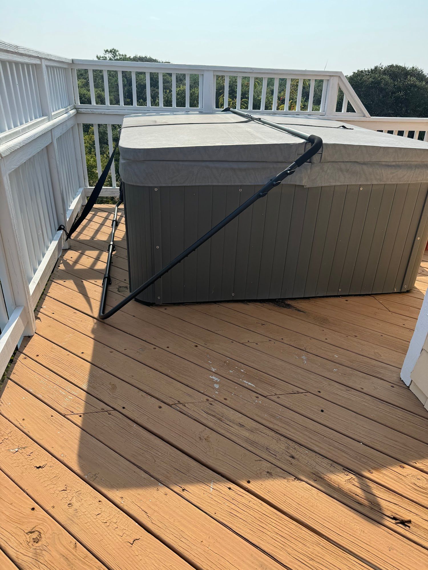 Hot tub on wooden deck, covered with gray lid and black support arms, white railing in background.