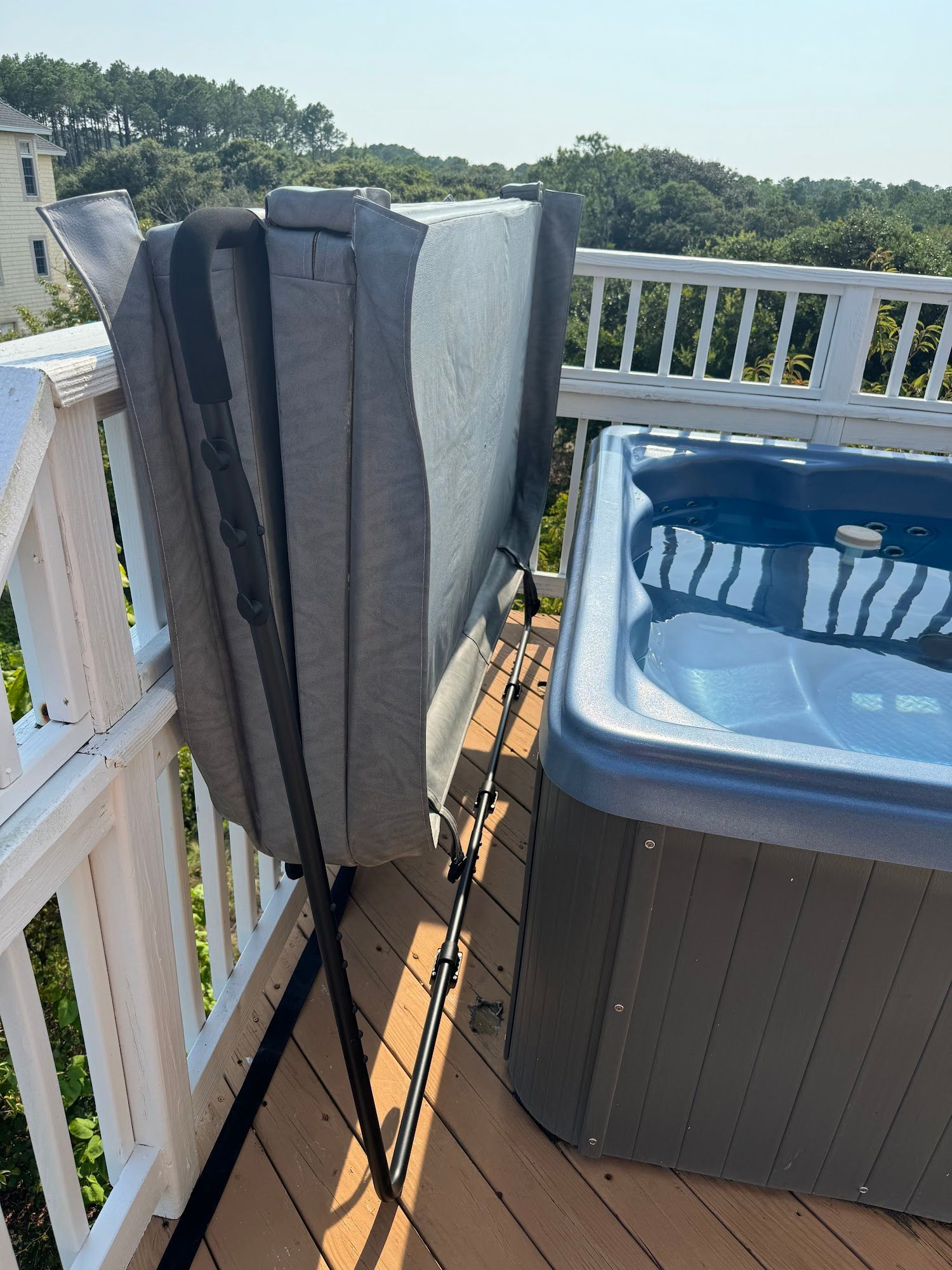 Hot tub with folded cover on a deck, wooden railing, trees in background, sunny day.