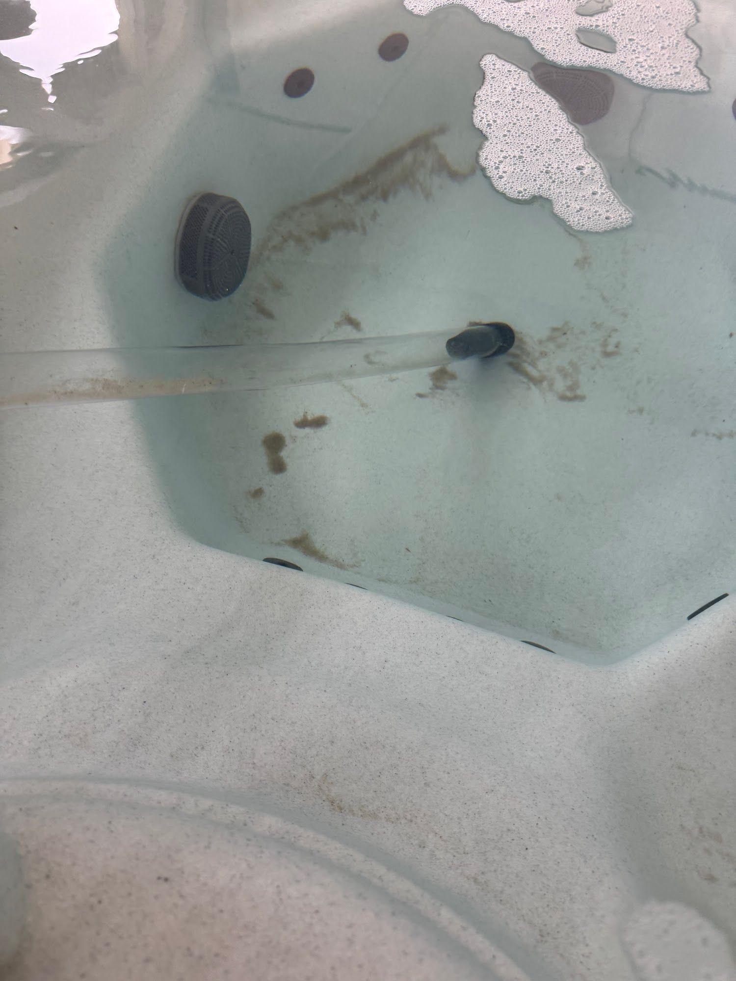 A close-up of the bottom of a hot tub with brown stains and a dark gray outlet.