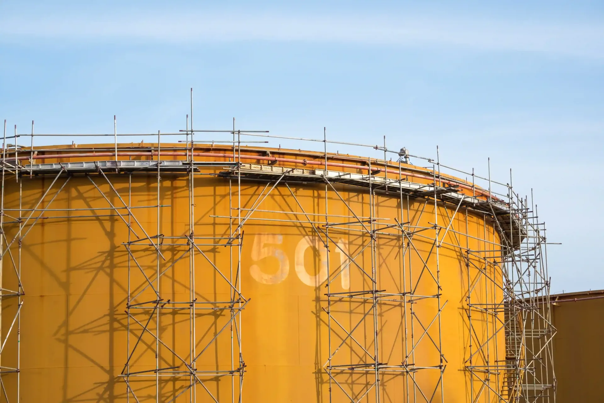 A large yellow industrial storage tank surrounded by metal scaffolding during a storage tank fabrica