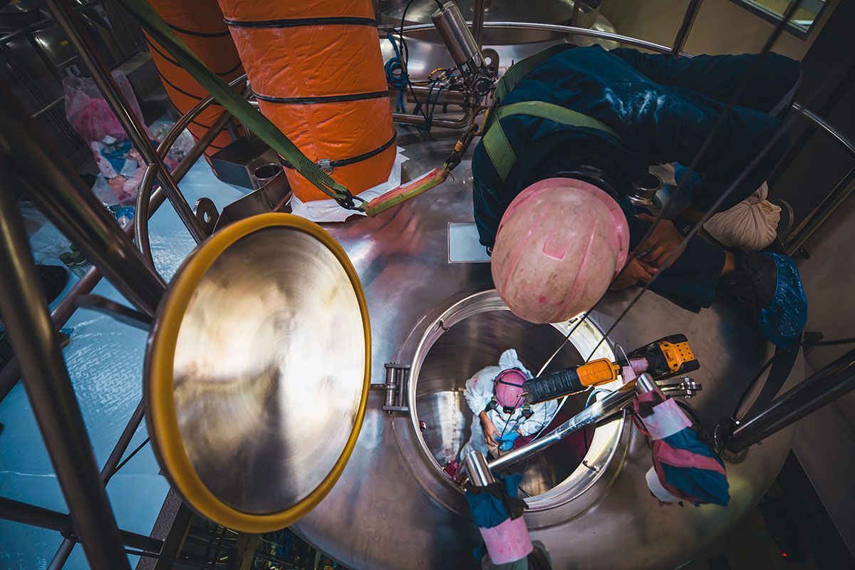 Top-down industrial photo showing a confined-space inspection on a stainless steel storage vessel, p