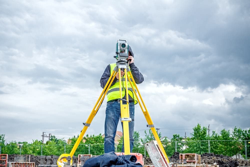 A Man Is Standing On A Tripod Looking Through A Telescope — Clarence Valley Surveys In Grafton, NSW
