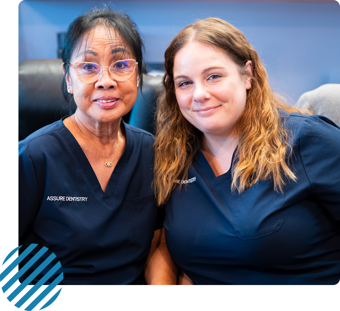 Two women in blue scrubs smiling, seated close together.