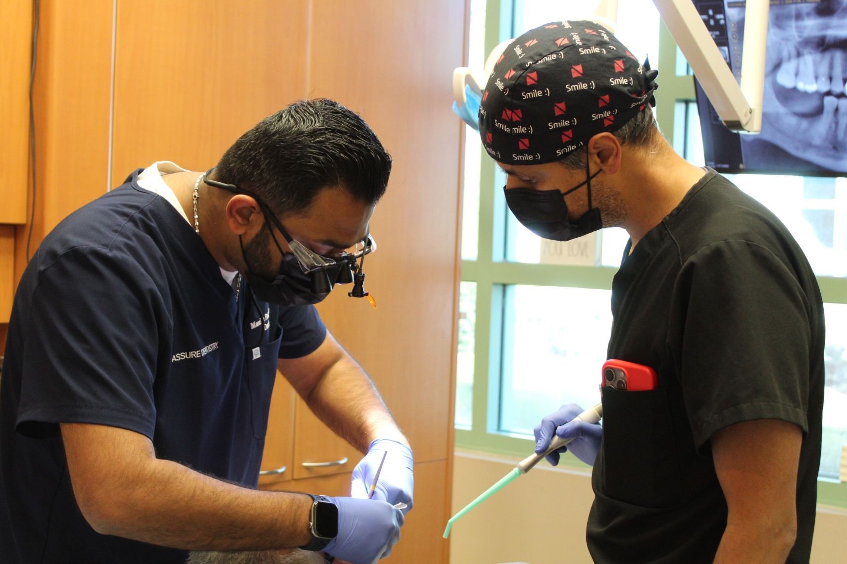 Two women in blue scrubs smiling, seated close together.