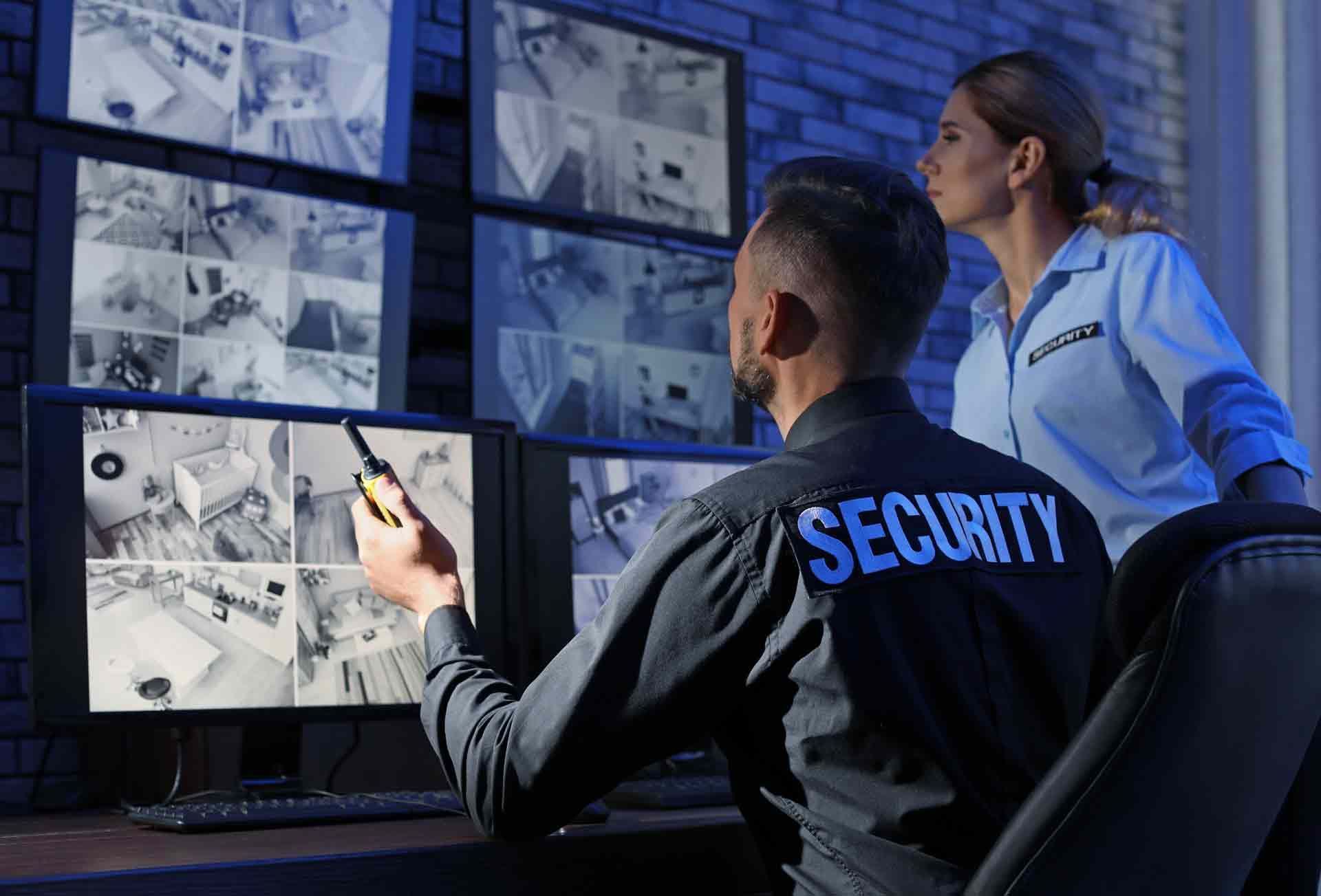 Security team monitoring surveillance cameras on multiple screens in control room.