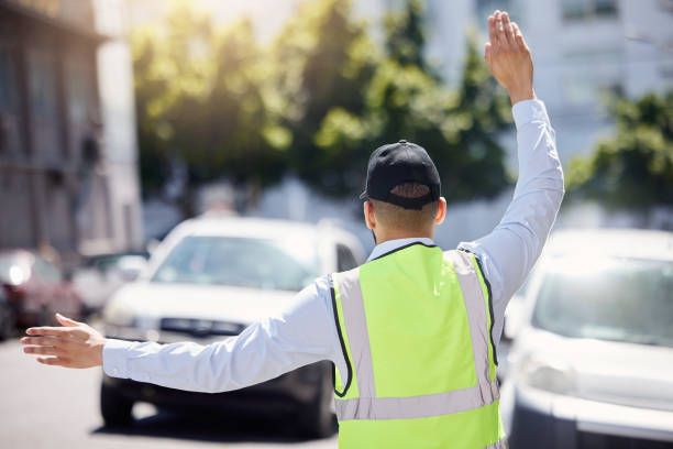 A man in a yellow vest is standing in the middle of a street with his arms outstretched.