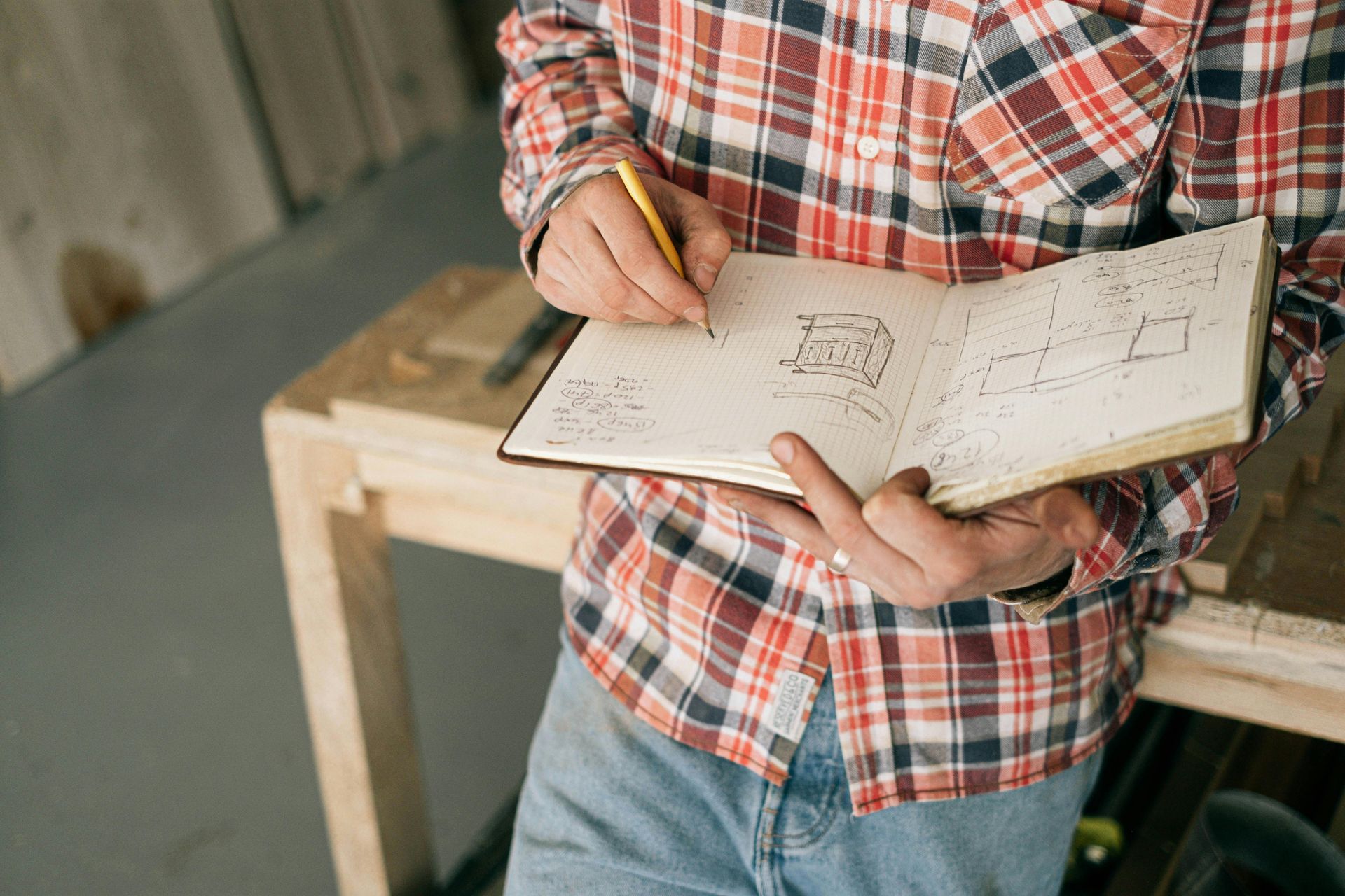 Un homme en chemise à carreaux tient un cahier et un crayon.
