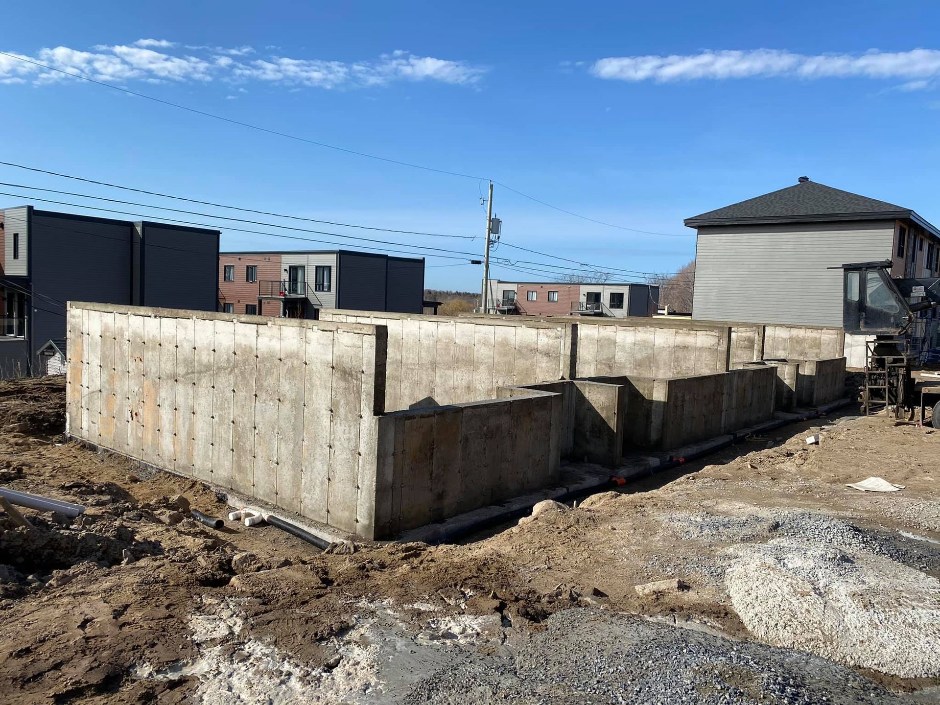 Un grand mur de béton est en train d'être construit dans un champ de terre devant une maison.