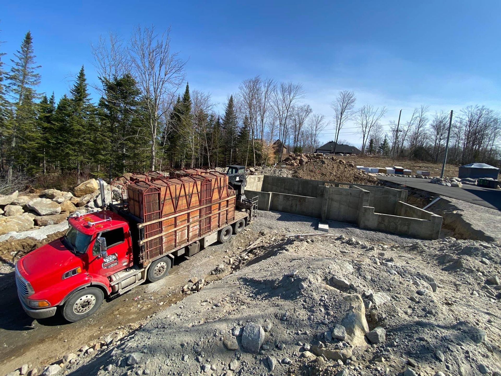 Un camion rouge roule sur un chemin de terre transportant des briques.