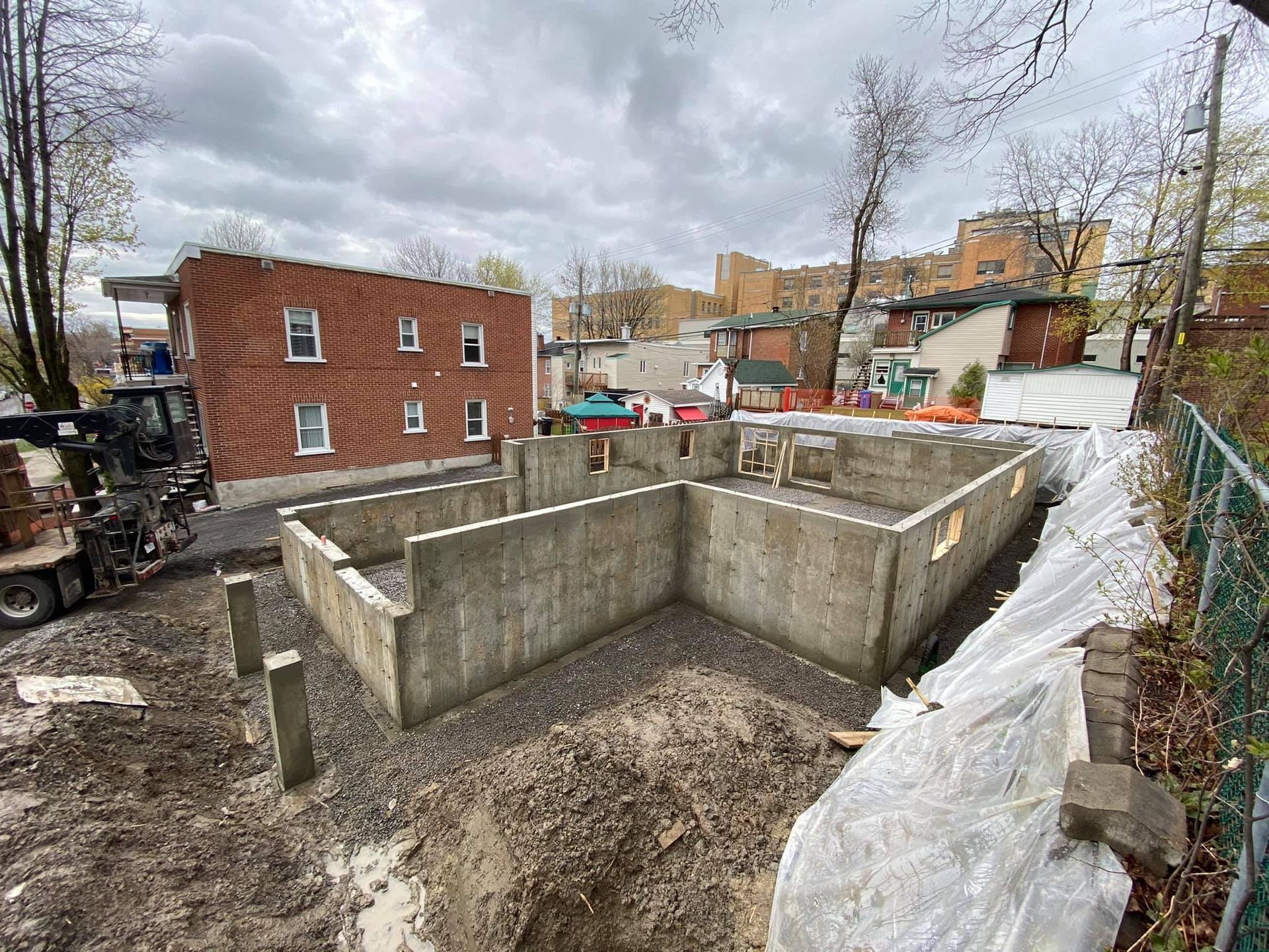 Une grande fondation en béton est en cours de construction devant un bâtiment en briques.