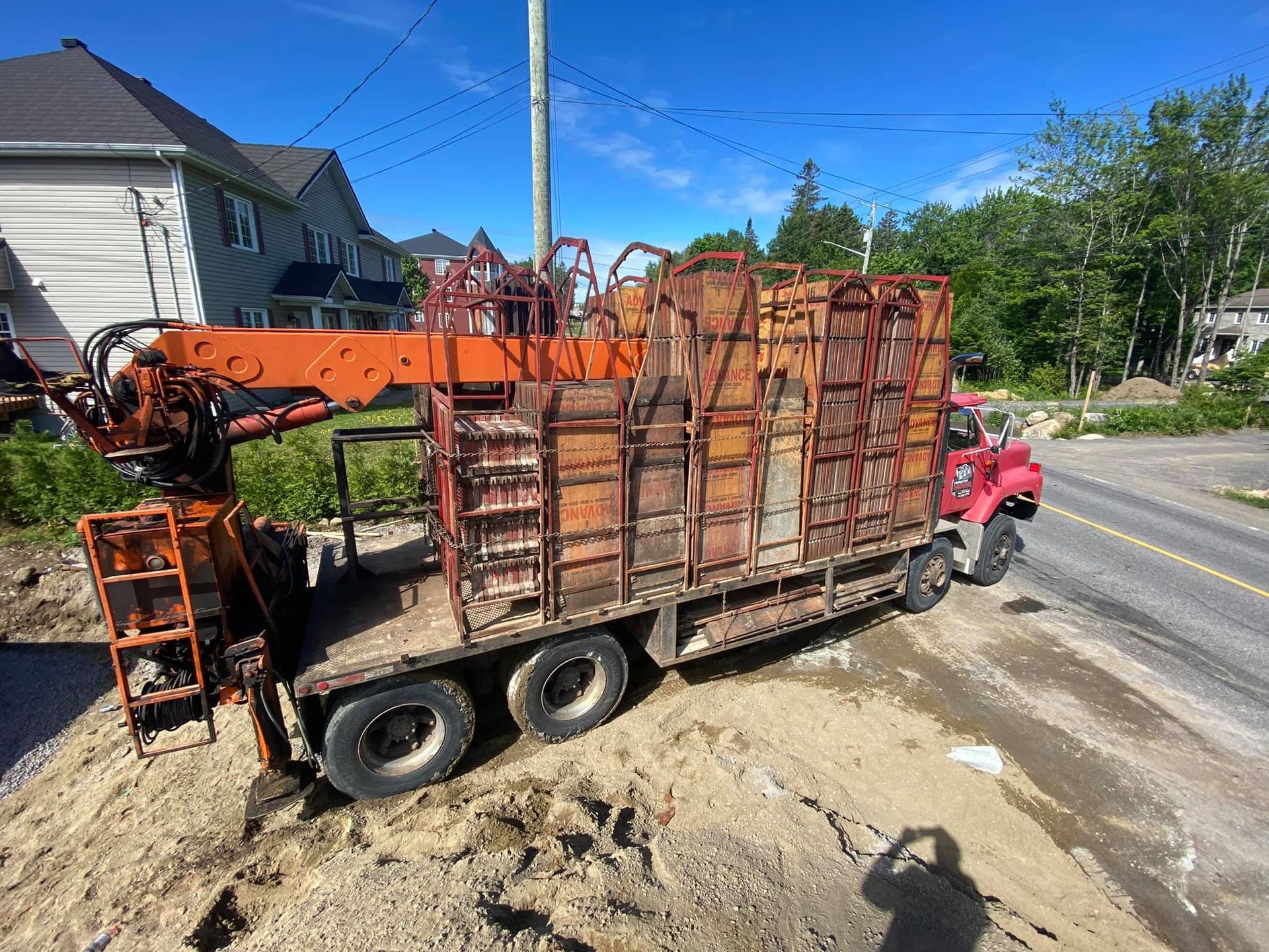 Un camion rouge avec une grue à l'arrière est garé sur le bord de la route.