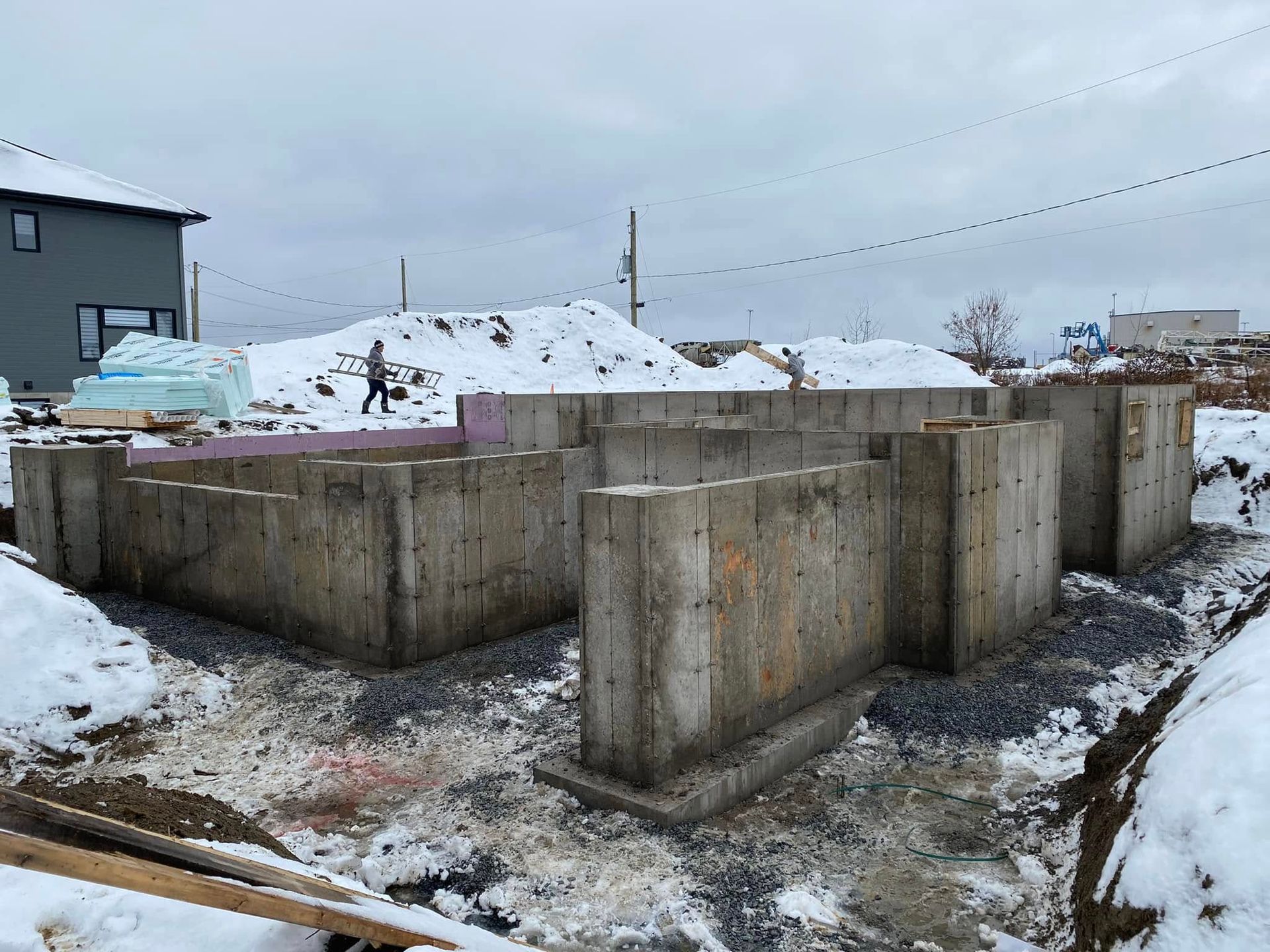 Un bâtiment en construction sous la neige avec une maison en arrière-plan.