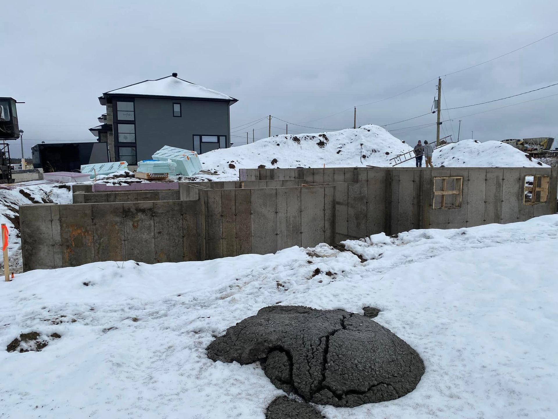 Un mur de béton est en cours de construction dans la neige avec une maison en arrière-plan.