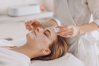cosmetologist performing face treatment applying face mask