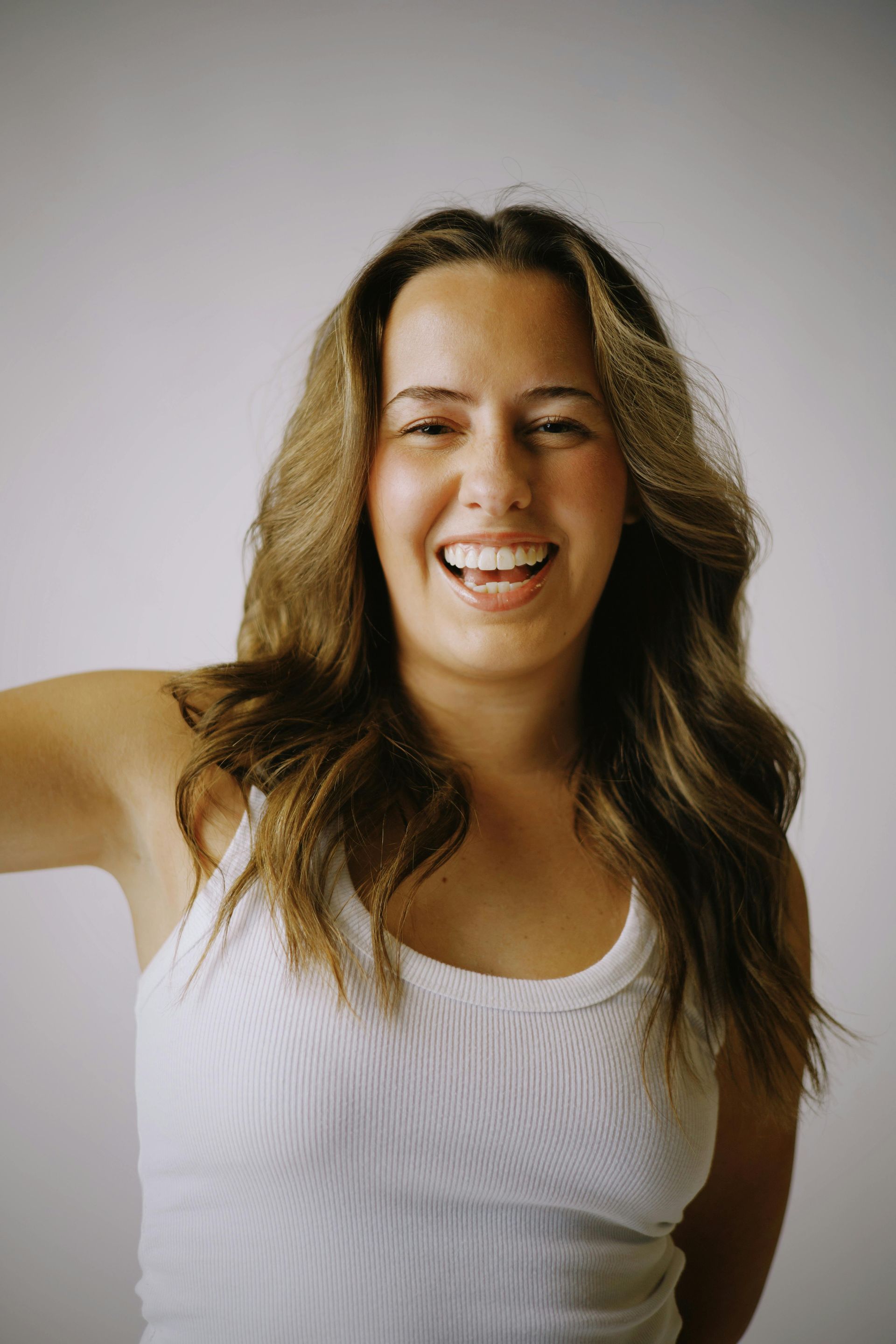 a woman in a white tank top smiles with her hand on her chin