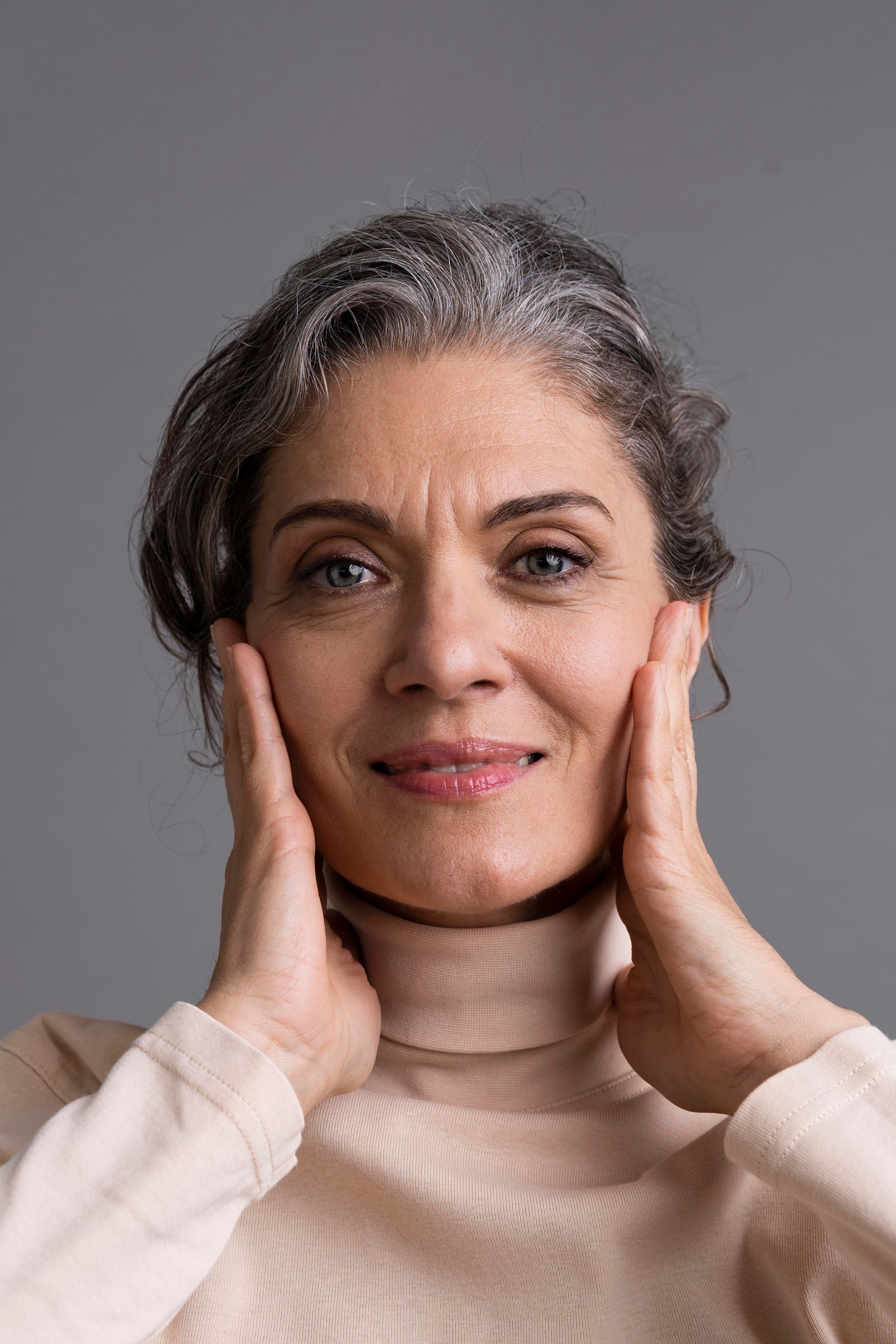 a woman with gray hair is smiling and touching her face