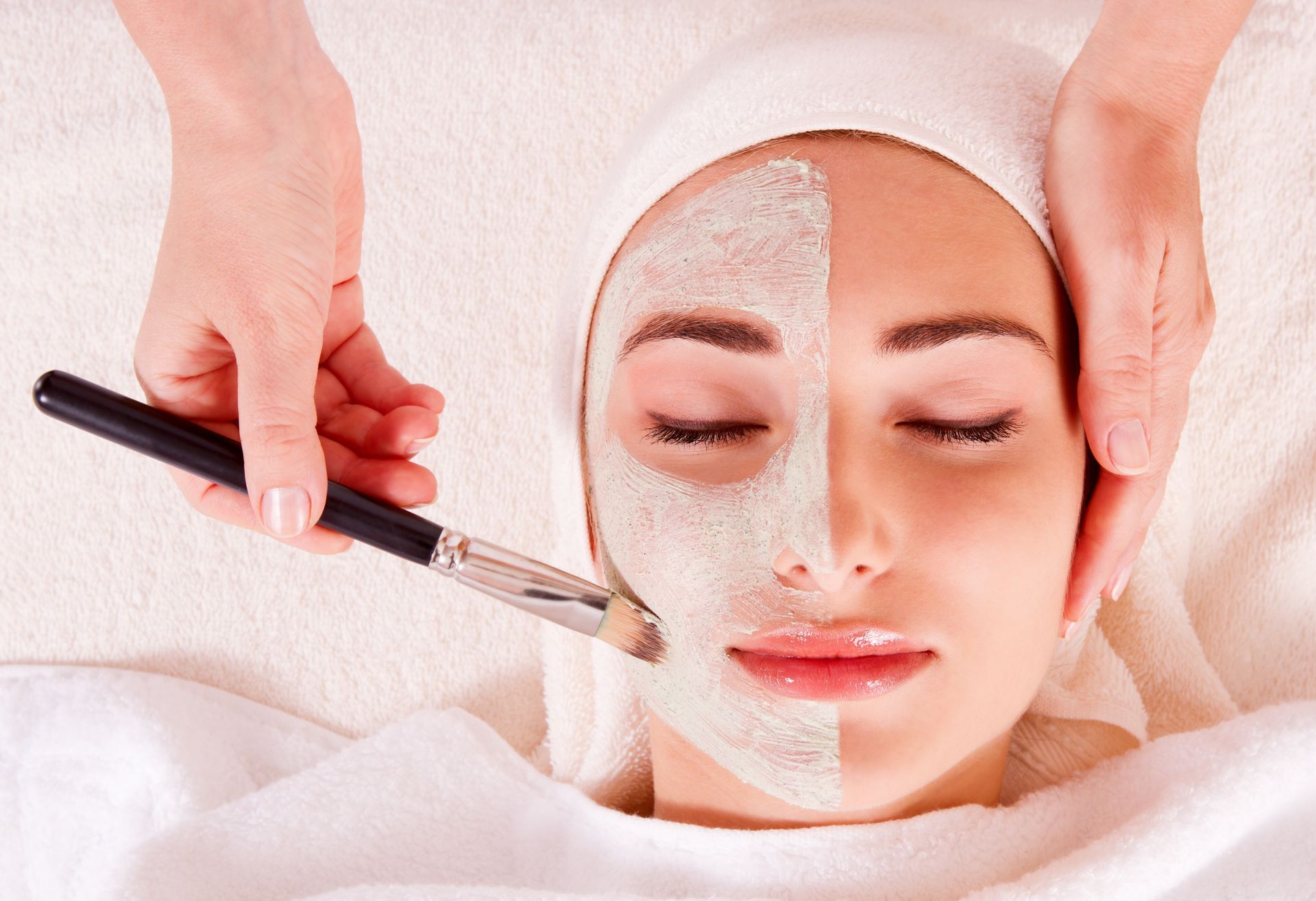 A woman is getting a facial treatment with a brush on her face.