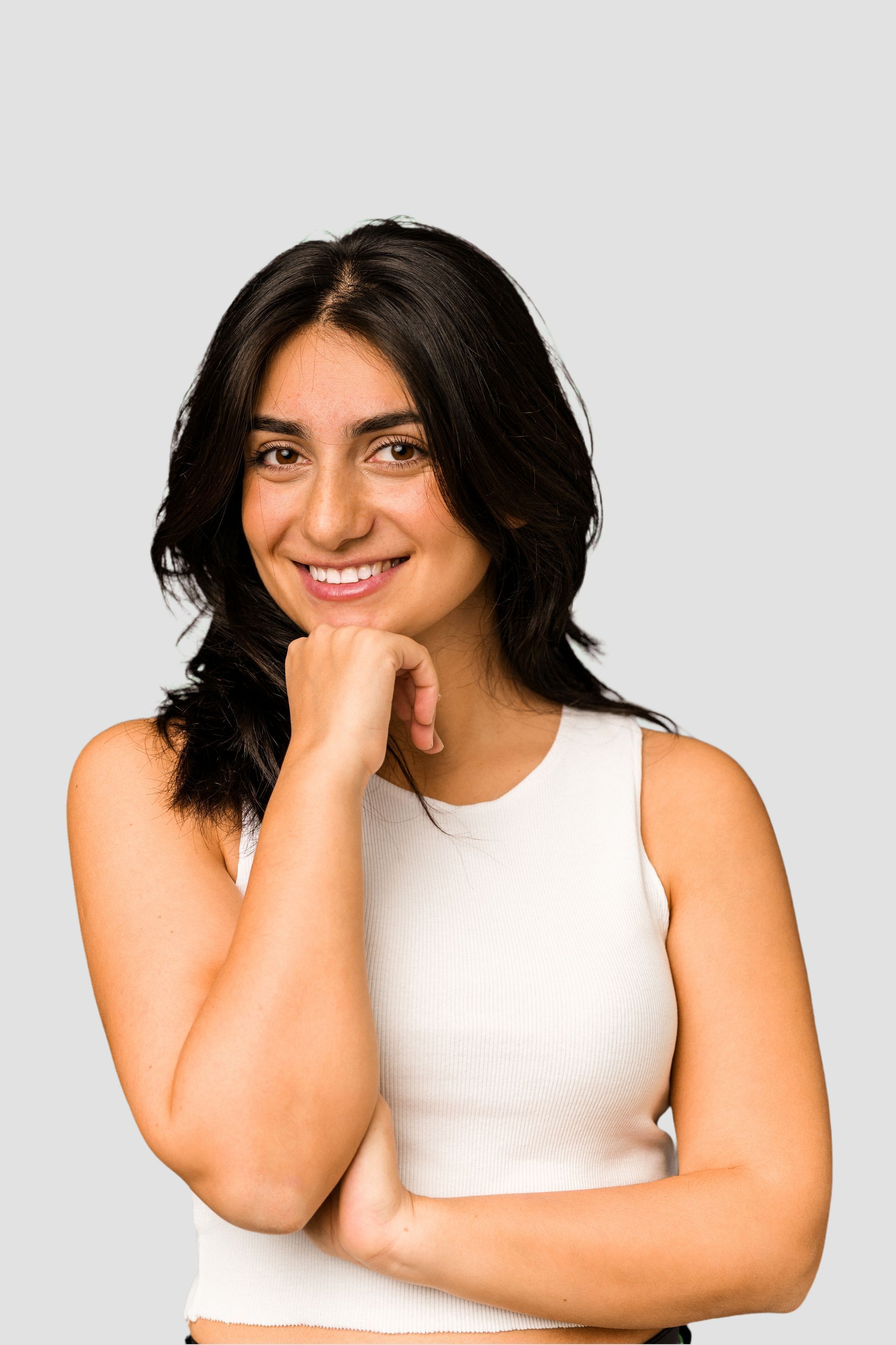 a woman in a white tank top smiles with her hand on her chin