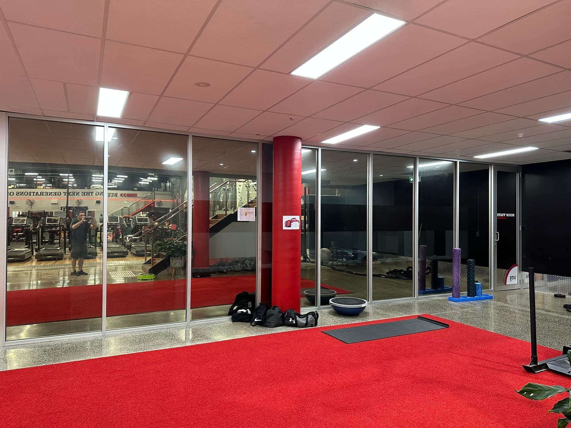 Red-carpeted gym interior with mirrored walls. Weight equipment visible. Bright overhead lighting — Wide Bay Tinting in Kensington, QLD