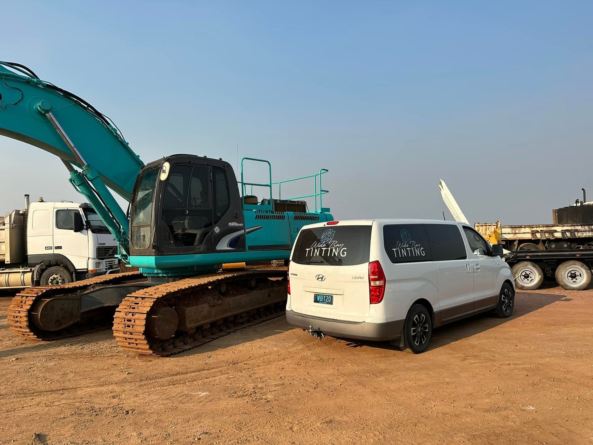 Excavator and white van parked on a dirt lot — Wide Bay Tinting in Kensington, QLD