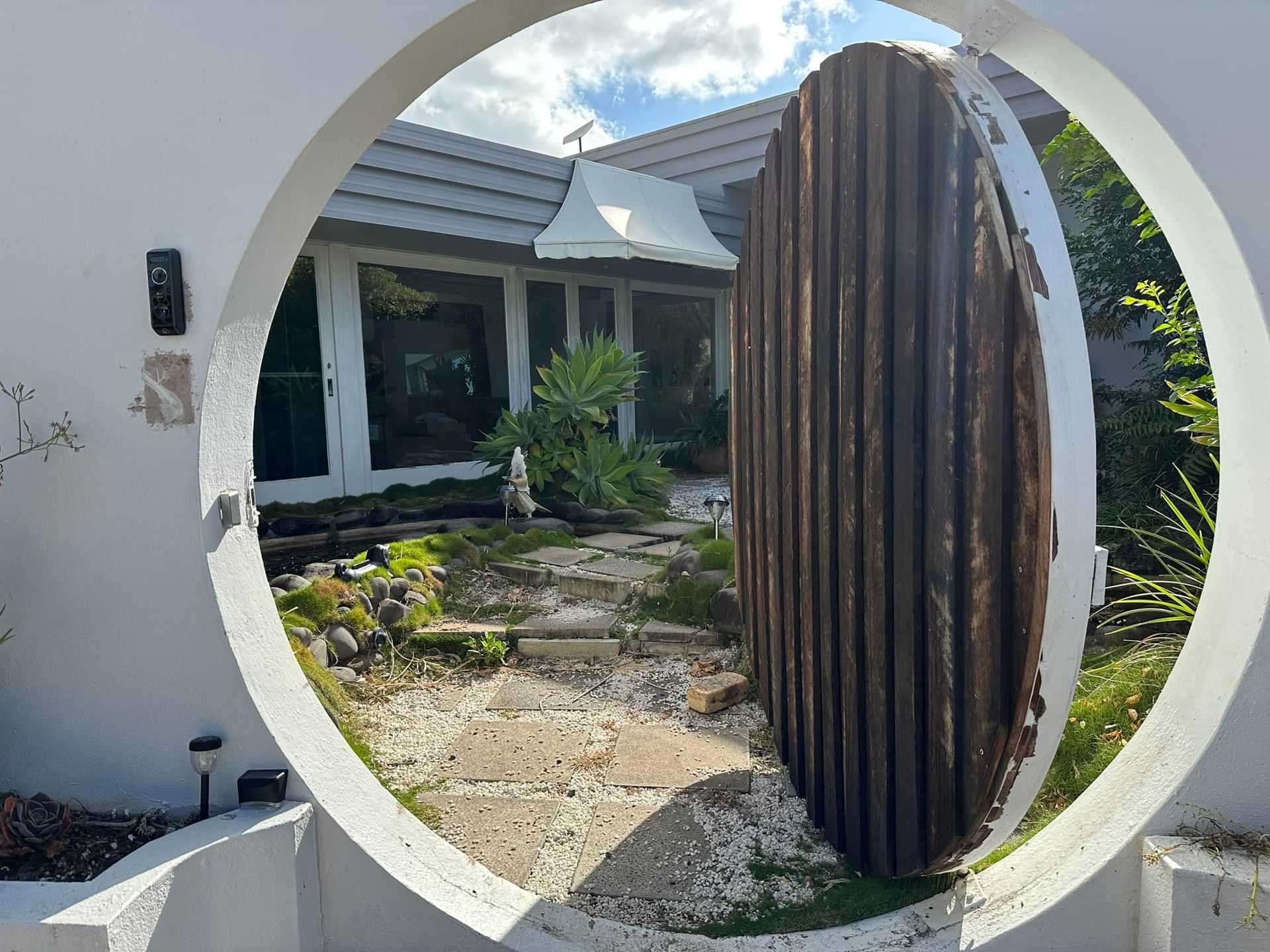 A circular entryway frames a stone path leading to a house with a decorative wooden sculpture — Wide Bay Tinting in Kensington, QLD