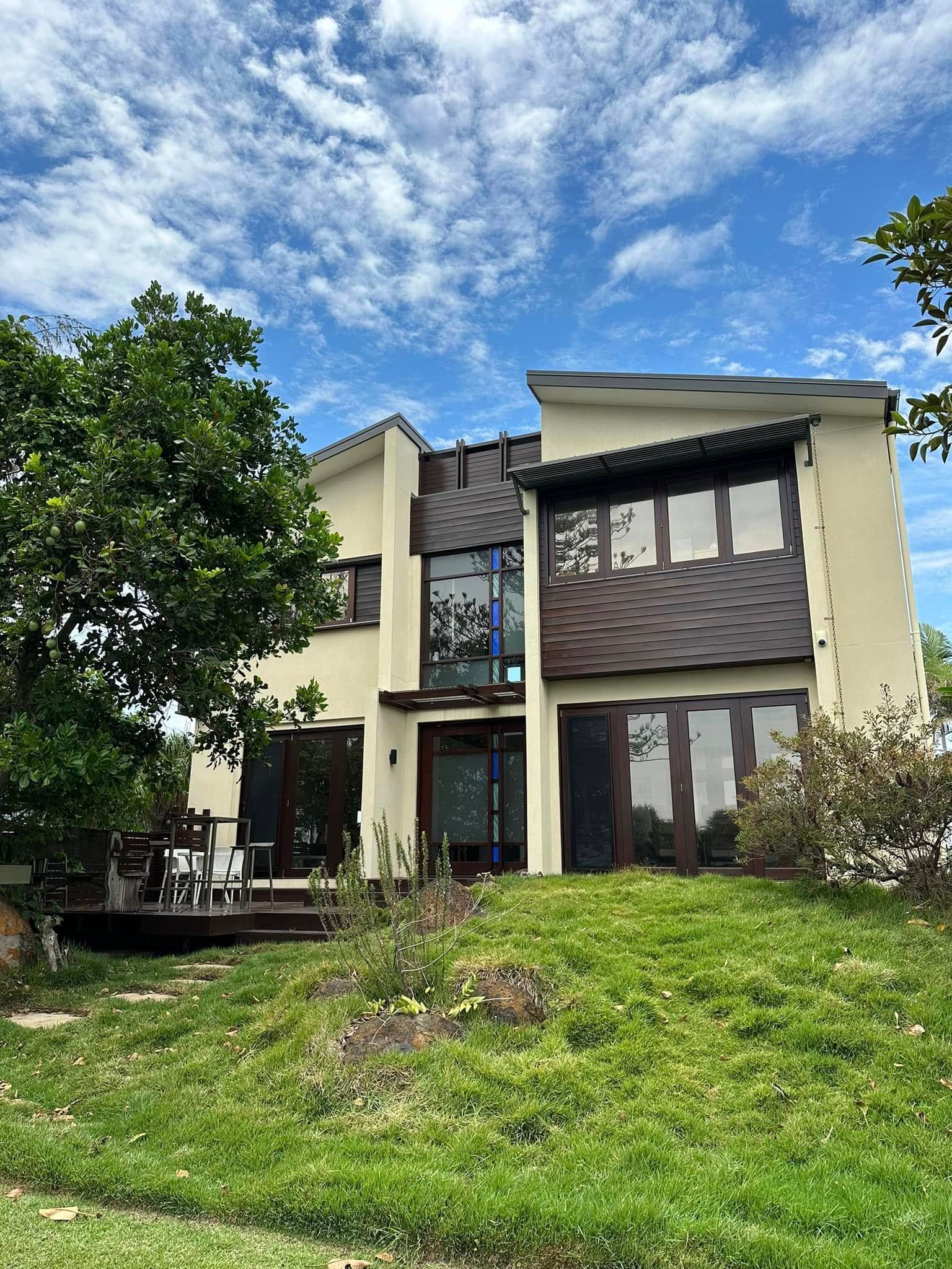 Two-Story House With Brown Roof and Beige Walls, in Front of a Green Lawn and Blue Sky — Wide Bay Tinting in Gin Gin, QLD