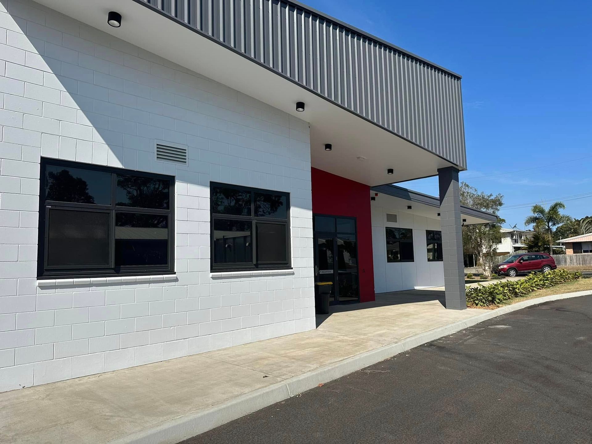 Exterior of a modern building with white block walls, dark windows, and a black and red entrance — Wide Bay Tinting in Kensington, QLD