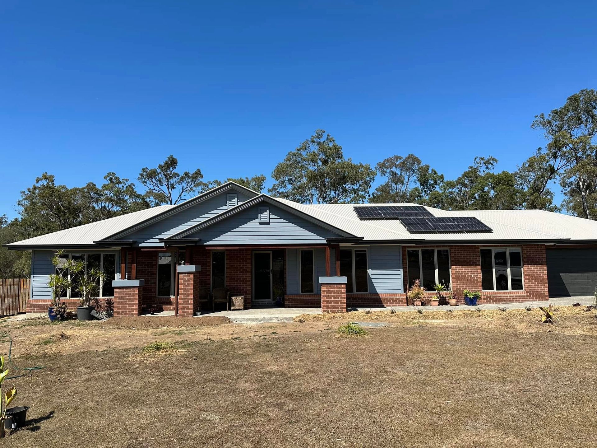 A one-story brick and blue siding house with a solar panel array on the roof — Wide Bay Tinting in Kensington, QLD