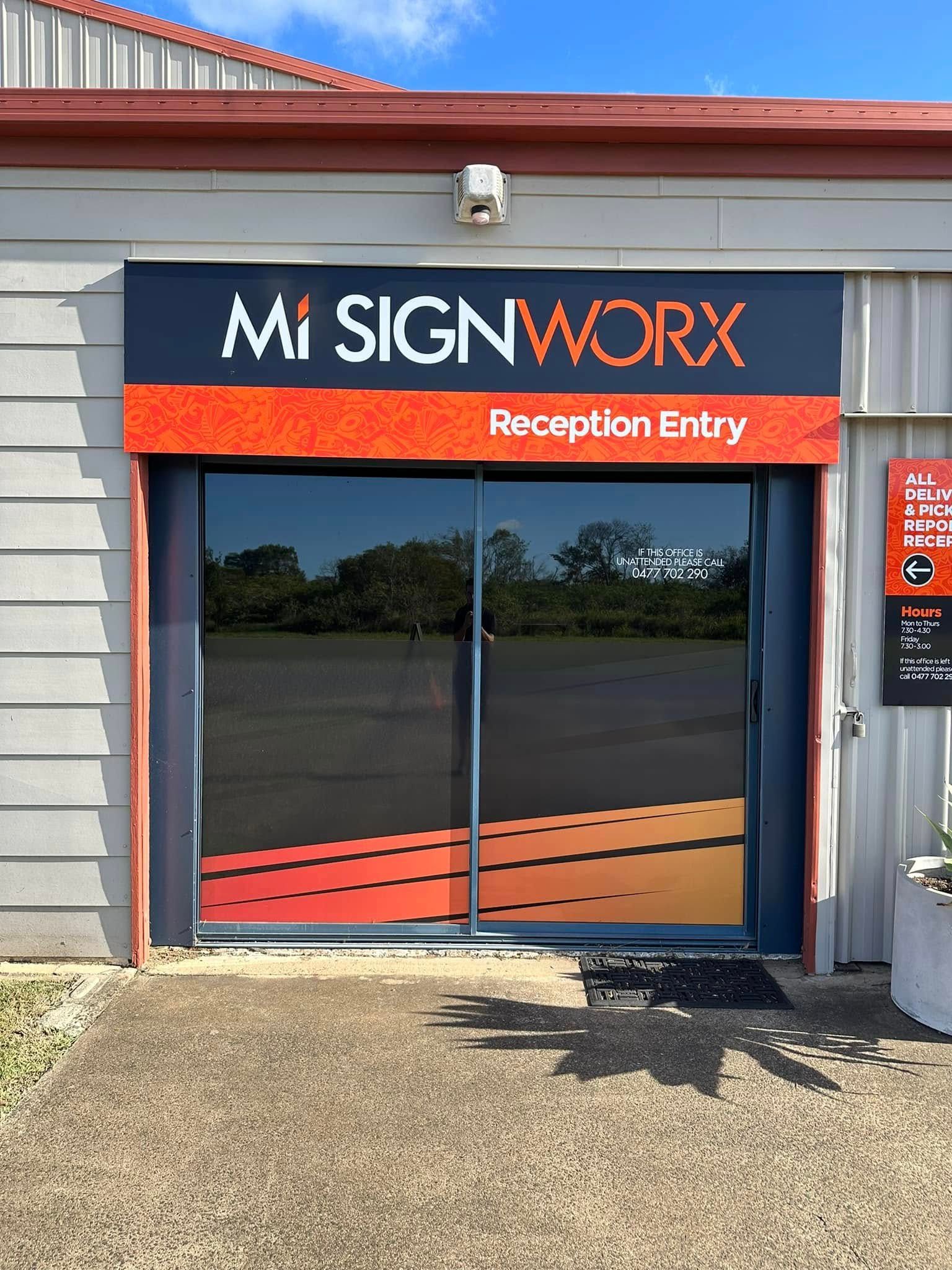 Entrance to Mi Signworx, with orange and black signage. Dark tinted glass doors with an orange and yellow gradient design — Wide Bay Tinting in Childers, QLD