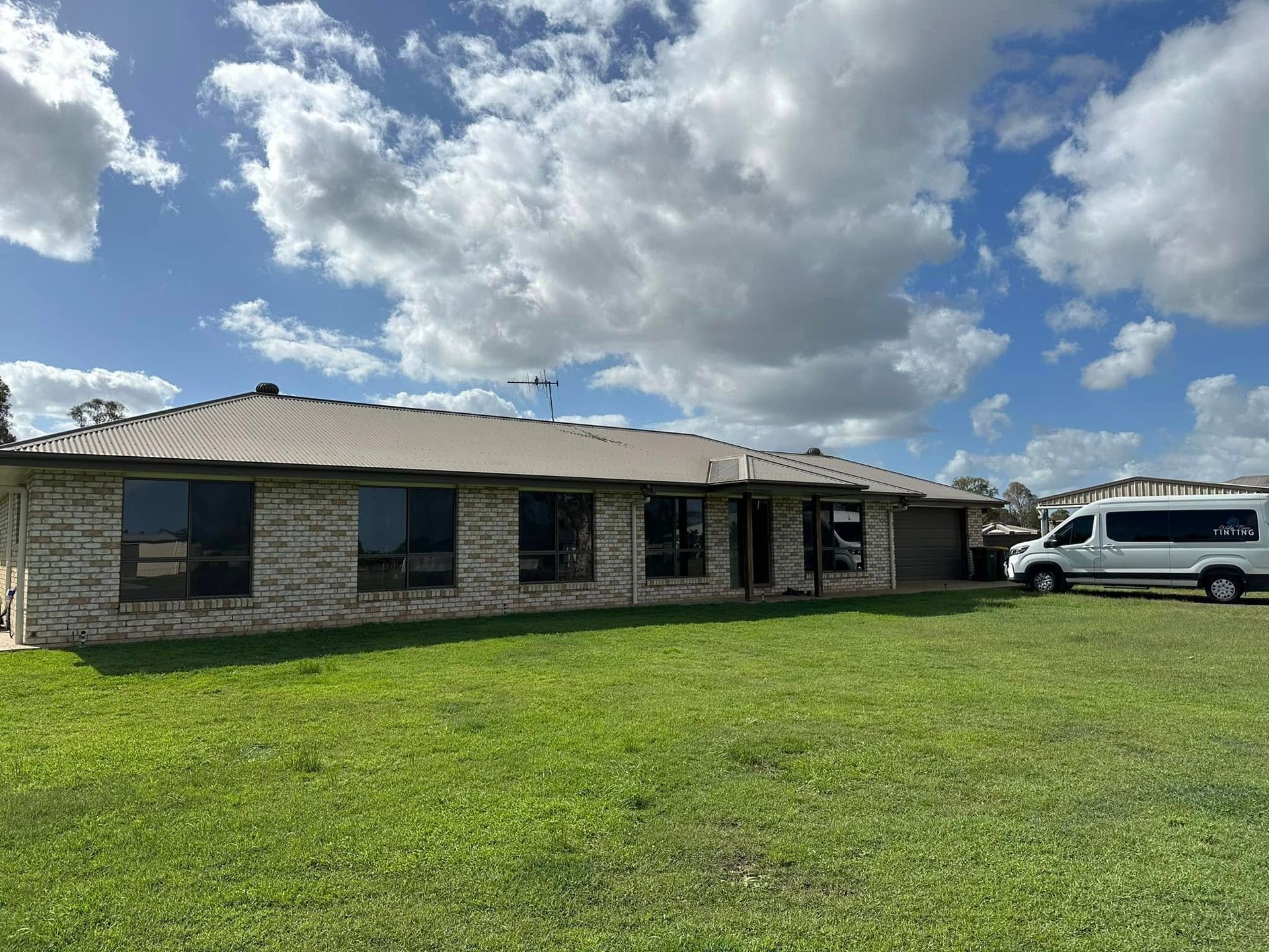 Single-story brick house with a brown roof and tinted windows, parked white van on the right — Wide Bay Tinting in Kensington, QLD