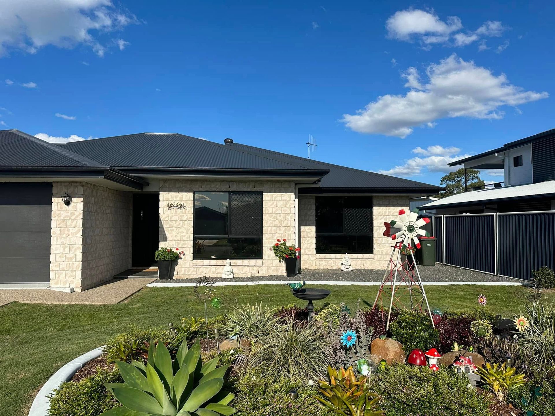 A Brick House With a Dark Roof and a Garden Under a Blue Sky With White Clouds — Wide Bay Tinting in Sharon, QLD