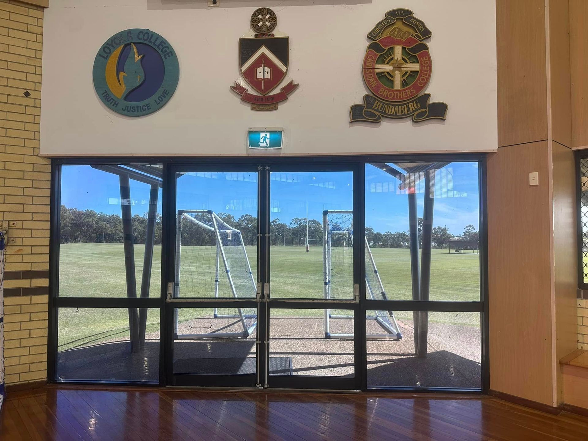Glass Doors Open to a Sports Field, With School Emblems Above — Wide Bay Tinting in Kensington, QLD