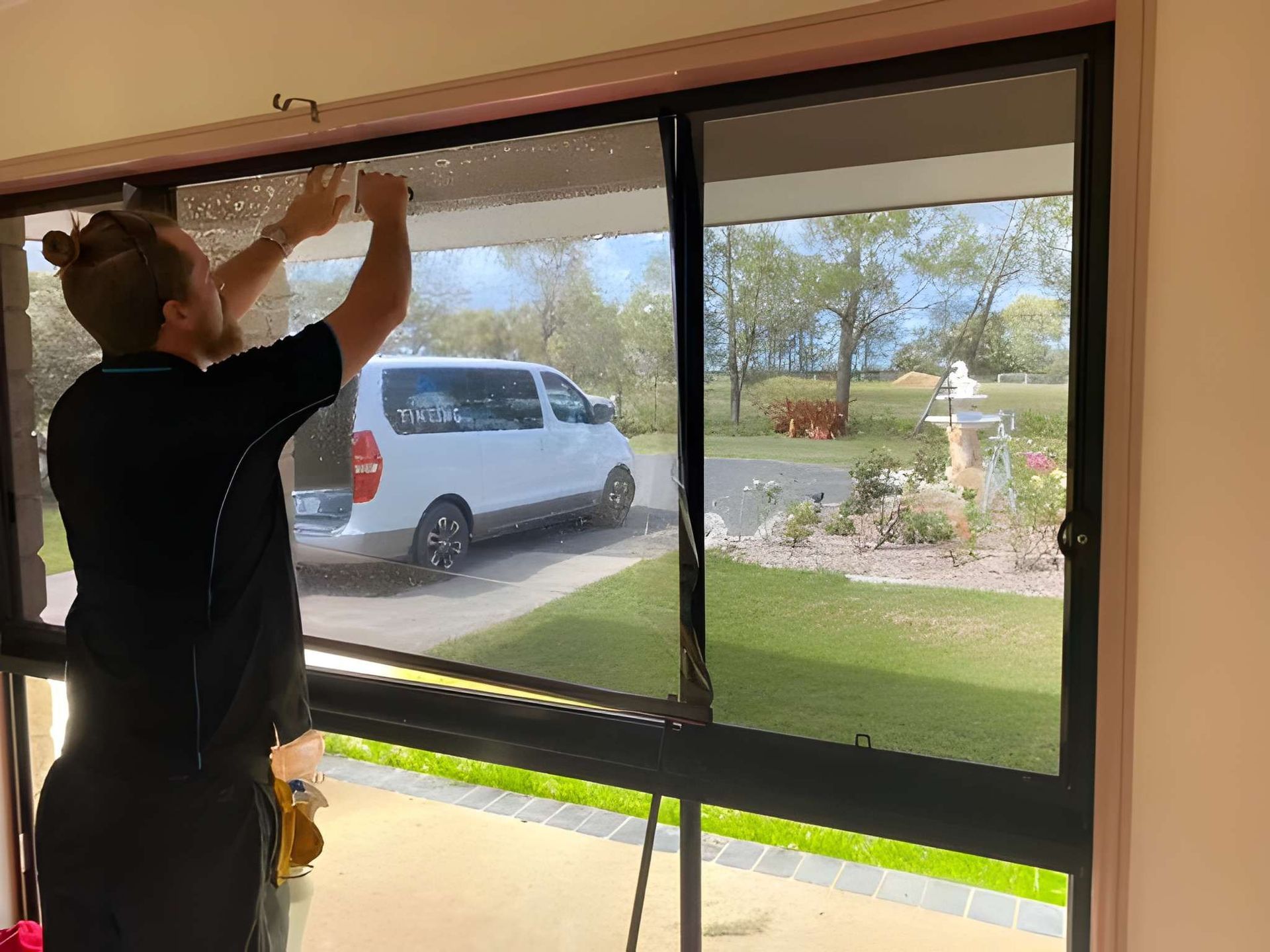 A Person Installing Window Film on a Sliding Glass Door in a Home — Wide Bay Tinting in Kensington, QLD