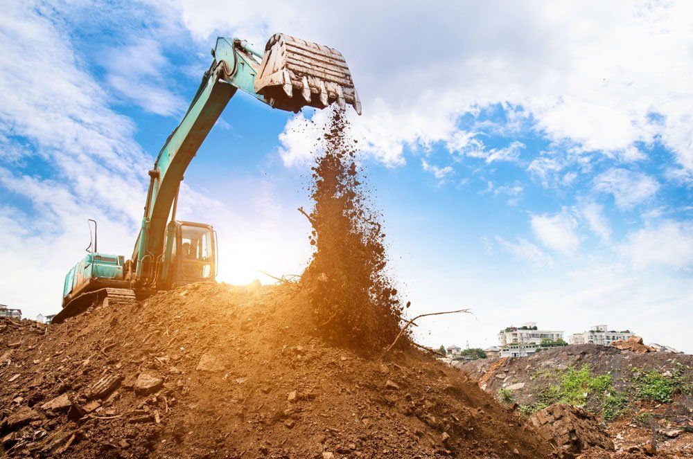 Excavator dumping soil onto a pile under a partly cloudy sky.