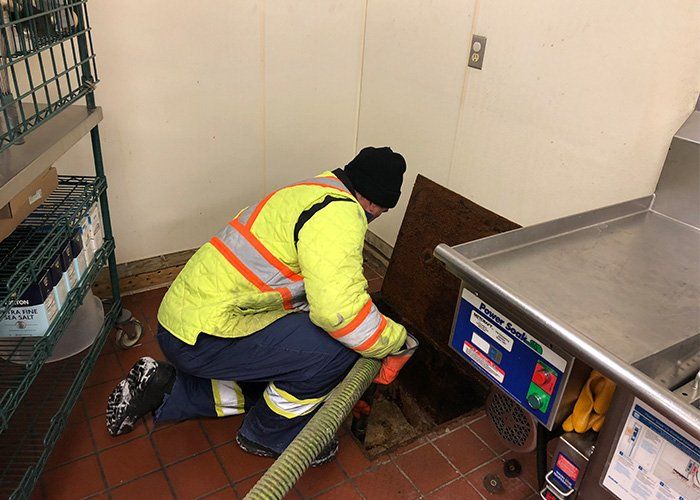 Person in safety vest cleaning a grease trap in a kitchen.