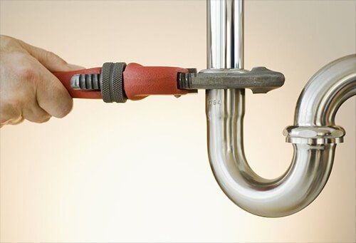 Hand tightening plumbing pipe with a red wrench, in a bright setting.