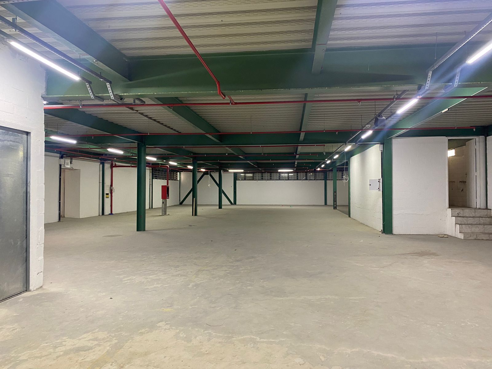 We Box Self Storage Um armazém vazio com piso de concreto e telhado metálico.