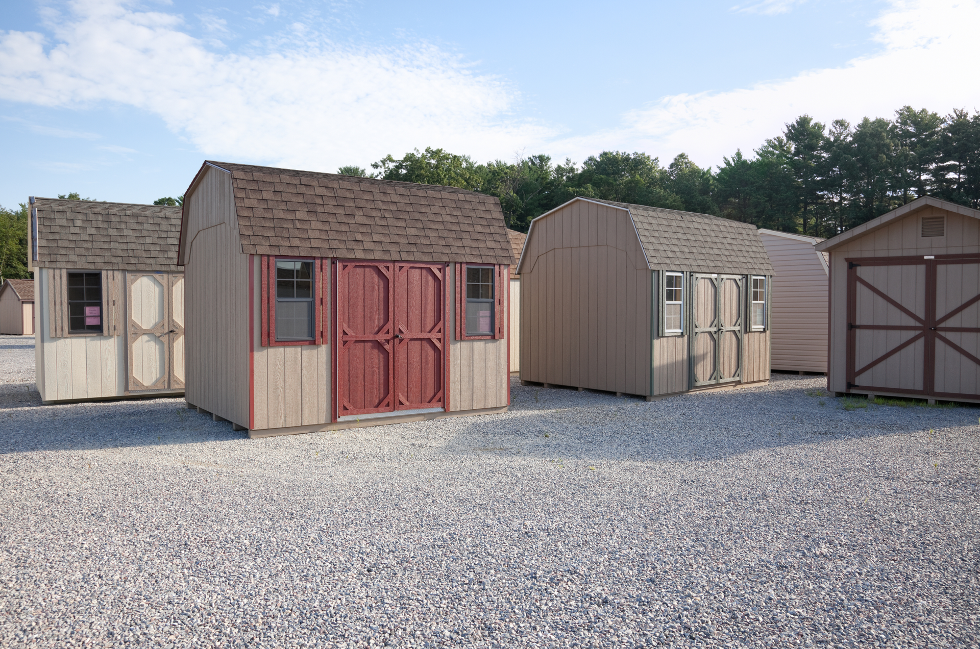Wooden storage sheds of various designs on a gravel lot.