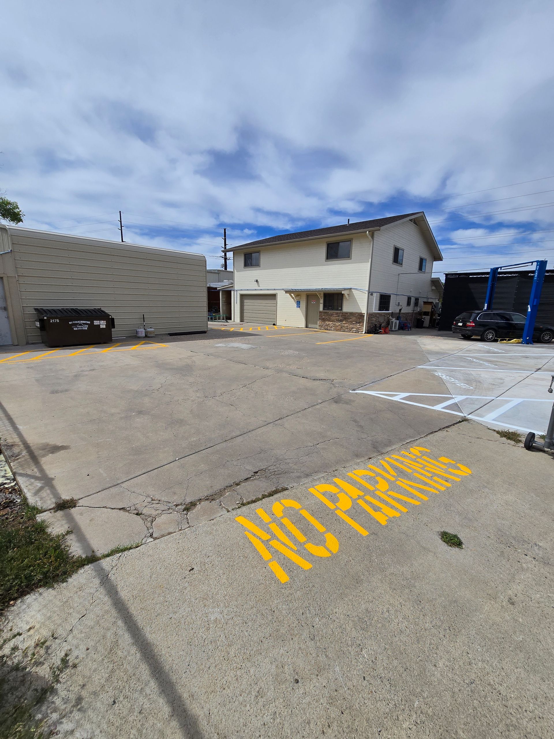 Parking lot with yellow “NO PARKING” marking, concrete building, and cloudy sky.