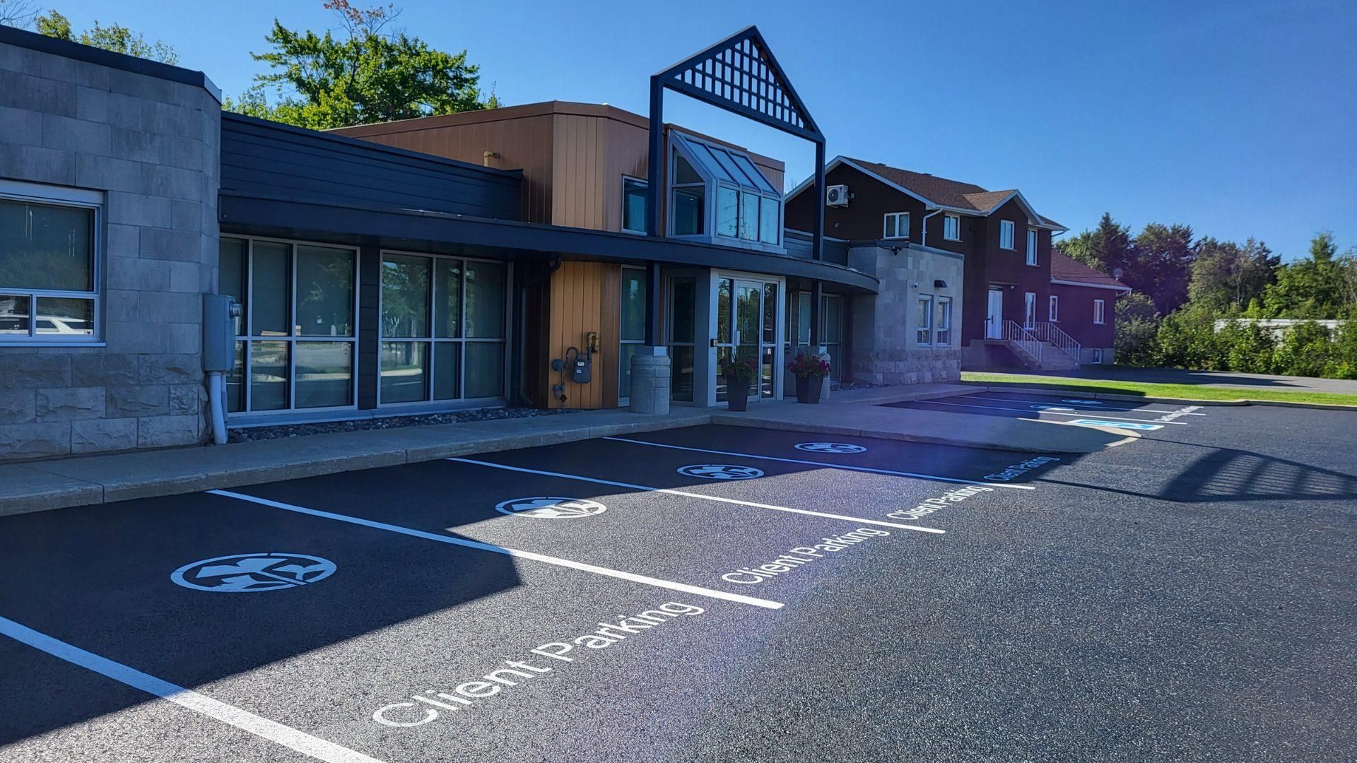 A yellow industrial roller flattens fresh asphalt on a construction site next to a gravel surface and an orange traffic cone.