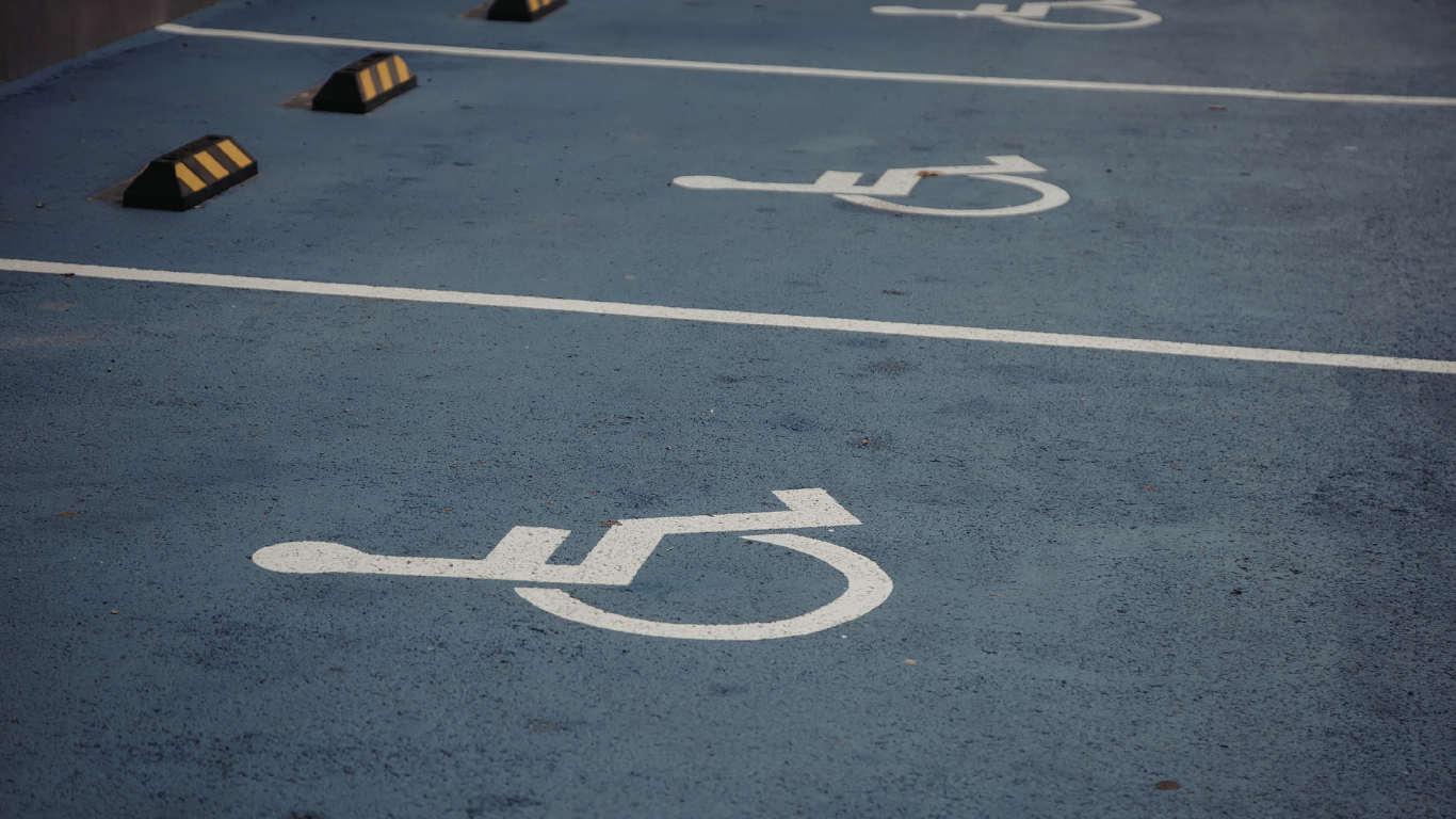 Accessible parking spaces marked with white wheelchair symbols painted on blue asphalt, featuring concrete wheel stops.