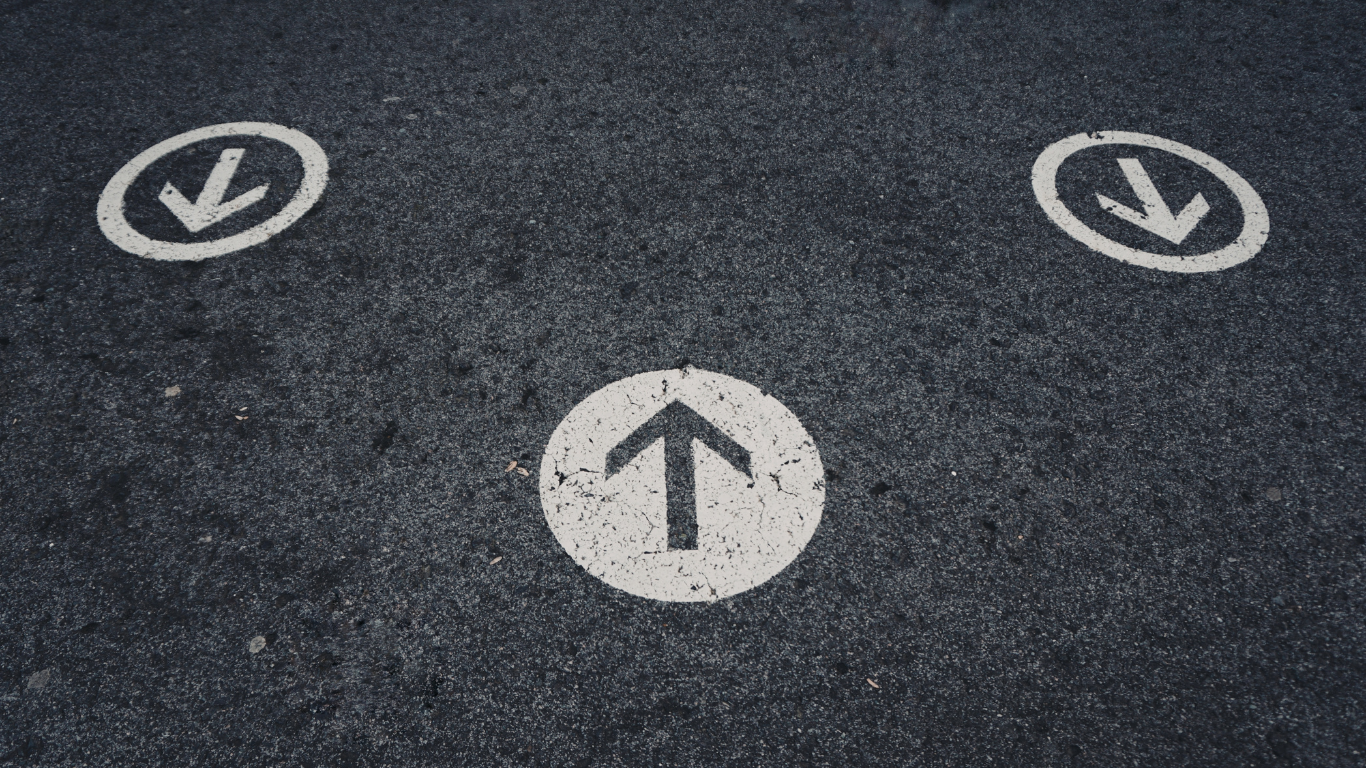 Three white circles painted on dark asphalt, each containing a black arrow; two point down and one points up.