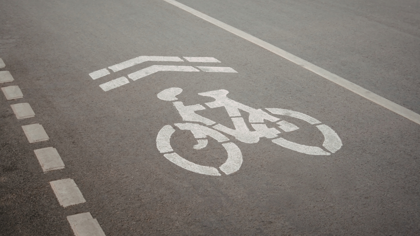 A white painted bicycle symbol with two chevron arrows above it on gray asphalt, marking a designated bike lane.