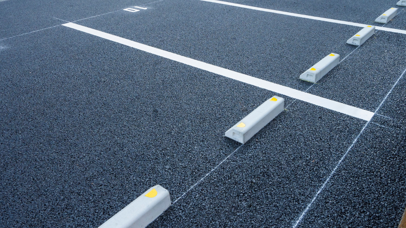 Empty parking spaces featuring white painted lines and concrete wheel stops on dark asphalt.