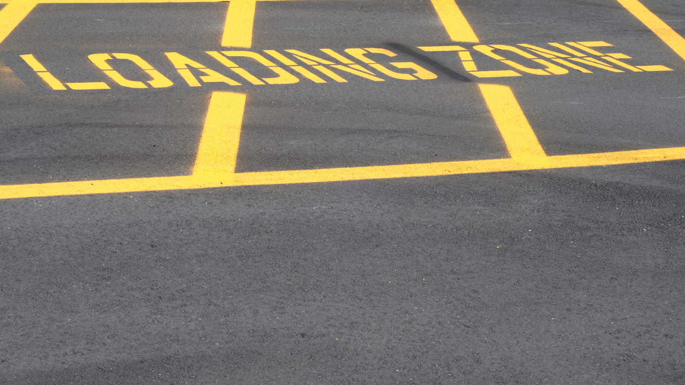 A worker in an orange vest and straw hat uses a concrete vibrator on fresh wet concrete poured into a steel rebar frame.