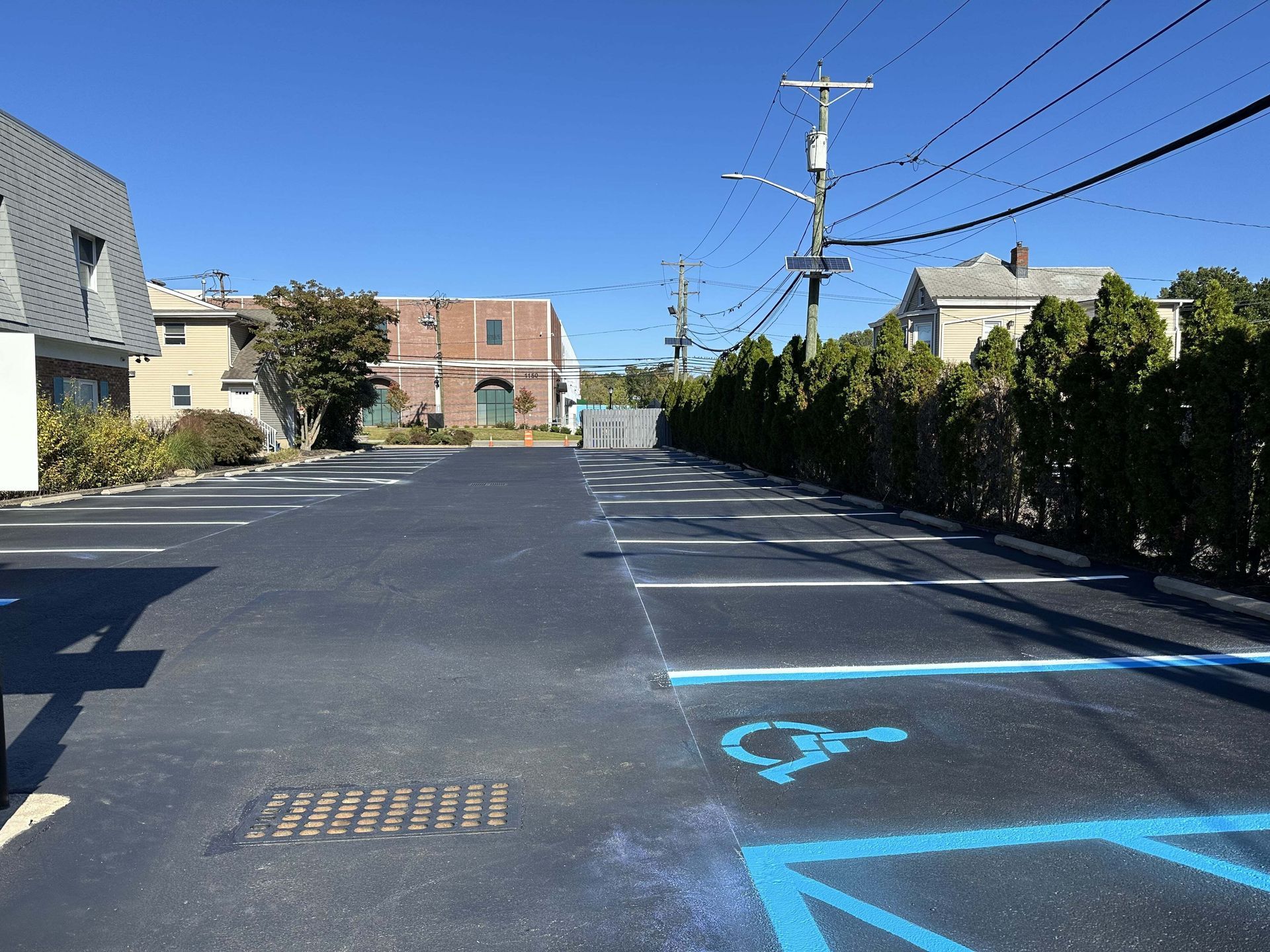A freshly paved parking lot in sunlight, featuring blue-painted accessible parking spaces with white striping.