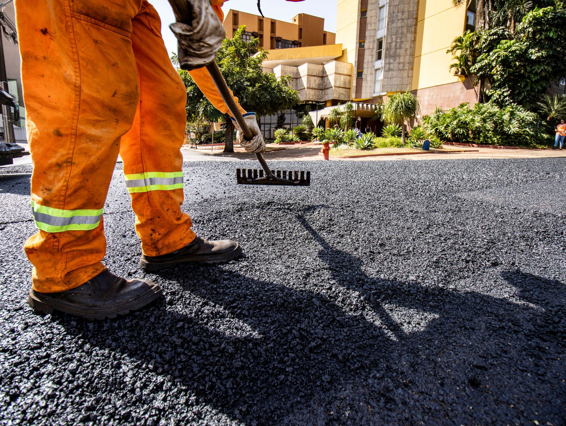 Worker spreading fresh asphalt on a driveway near apartment buildings and greenery