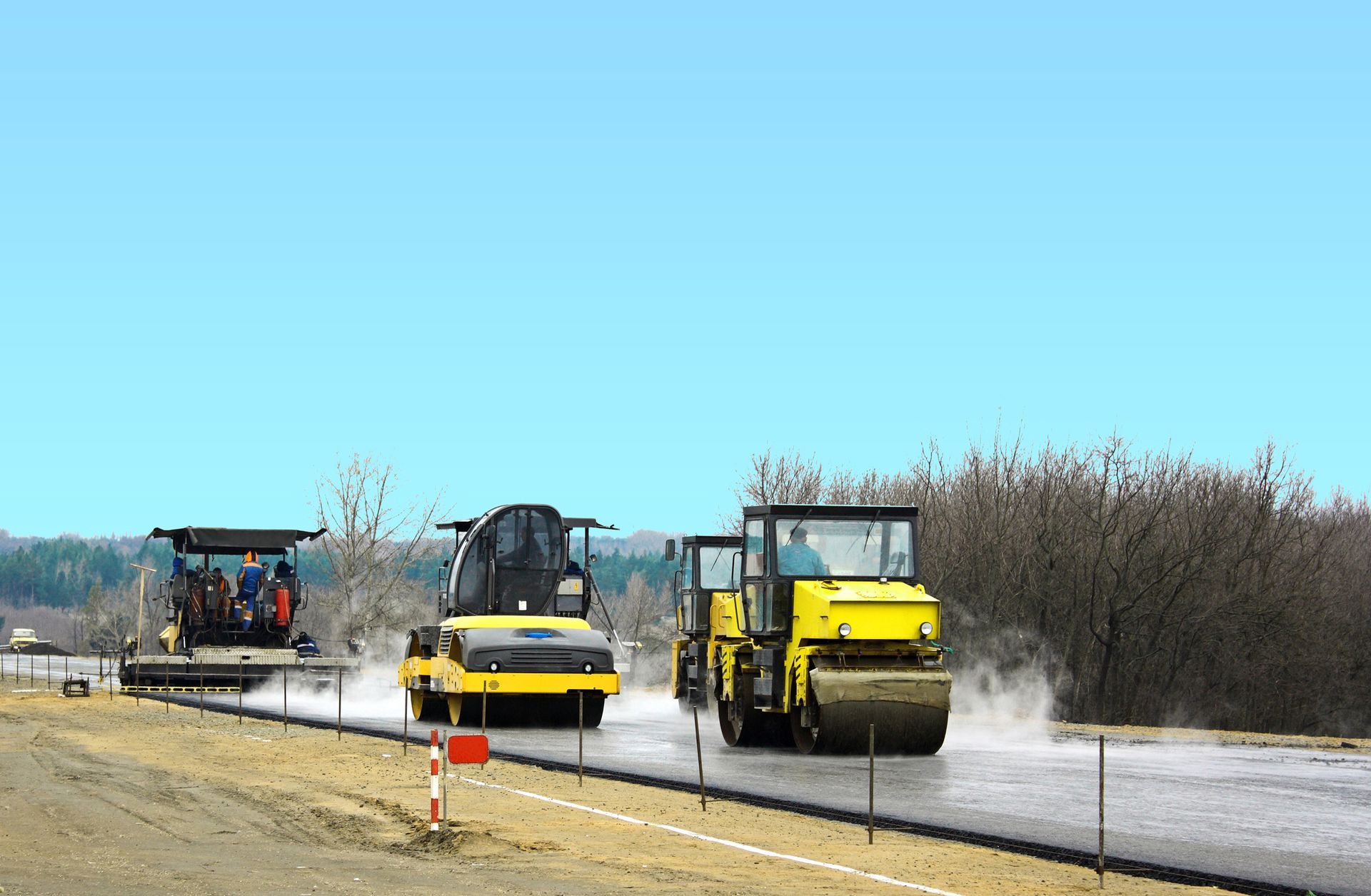 Three heavy construction machines paving a new road on a clear, sunny day.