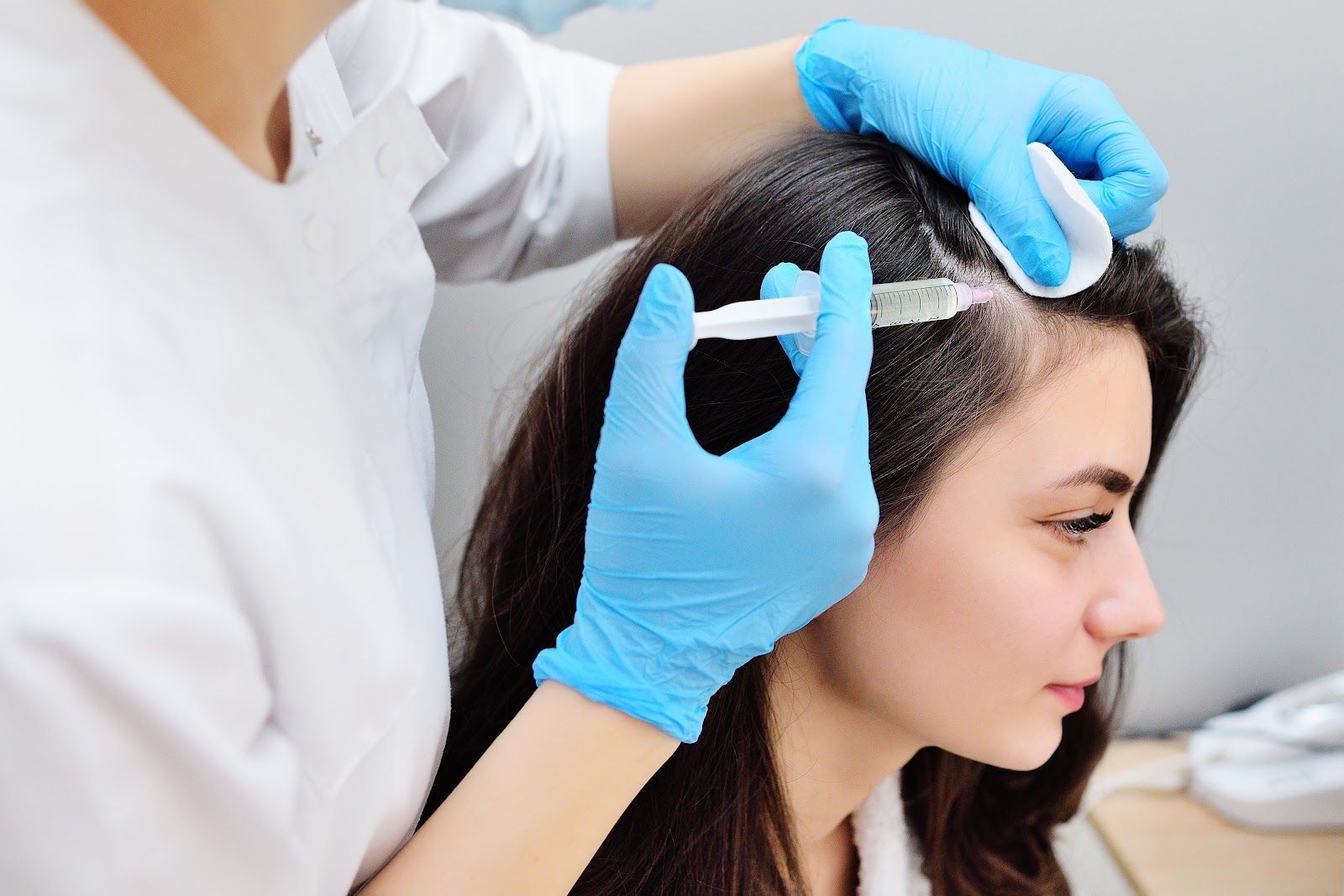 Person receiving scalp injection for hair treatment. Blue gloves, white coat, light background.