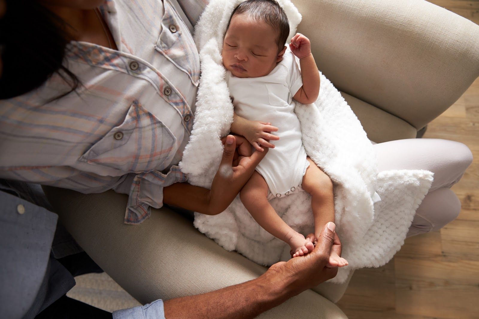 A person holding a sleeping baby wrapped in a white blanket on a light-colored couch.